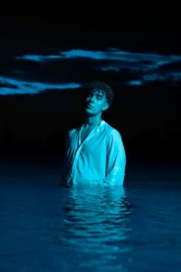 Man standing in dark water under blue clouds